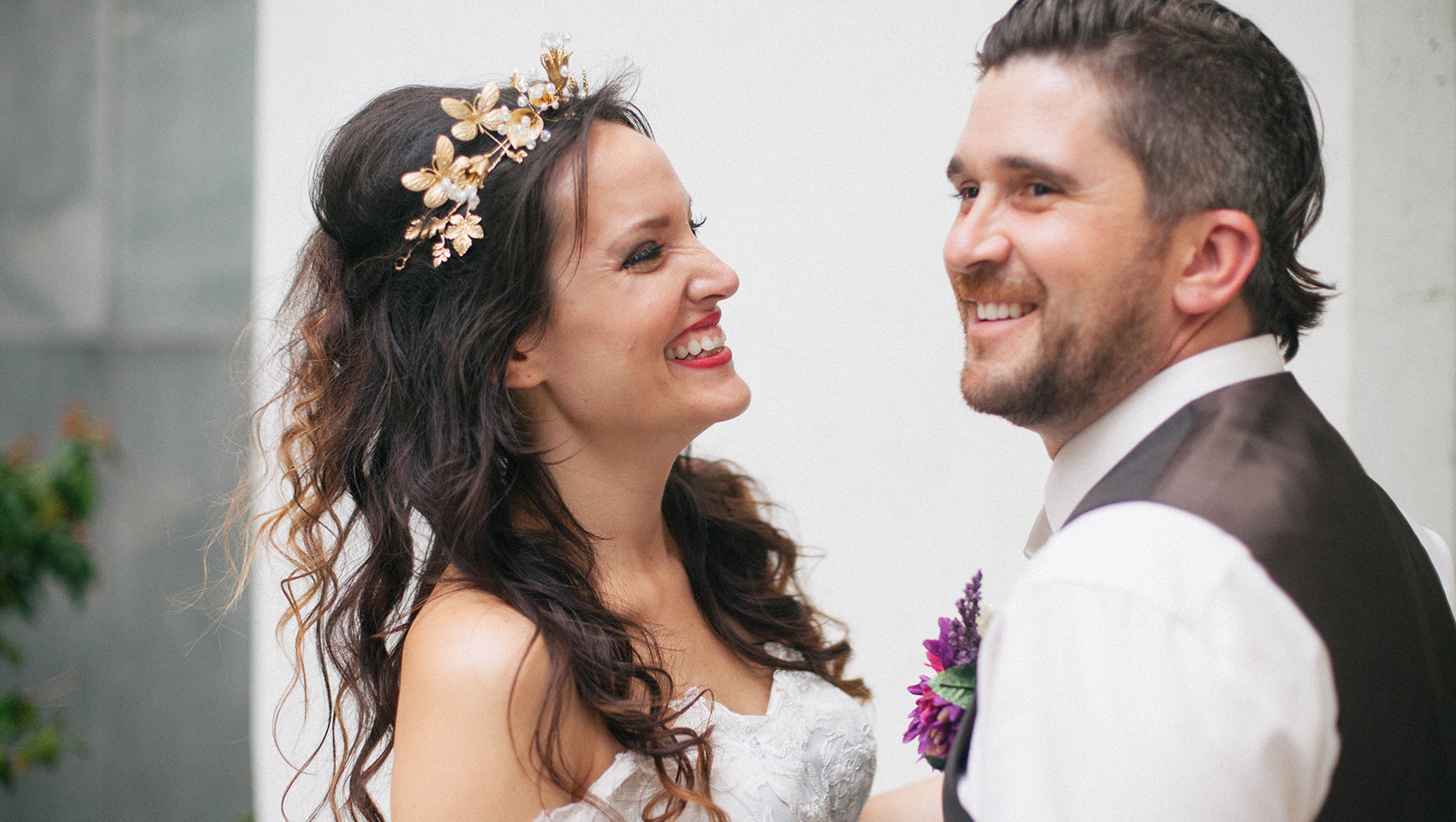 bride with flower crown smiling with groom in tuxedo vest